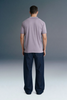 Full-length rear view of a man standing still, showcasing the fit and hang of a lavender polo shirt from behind against a grey background.