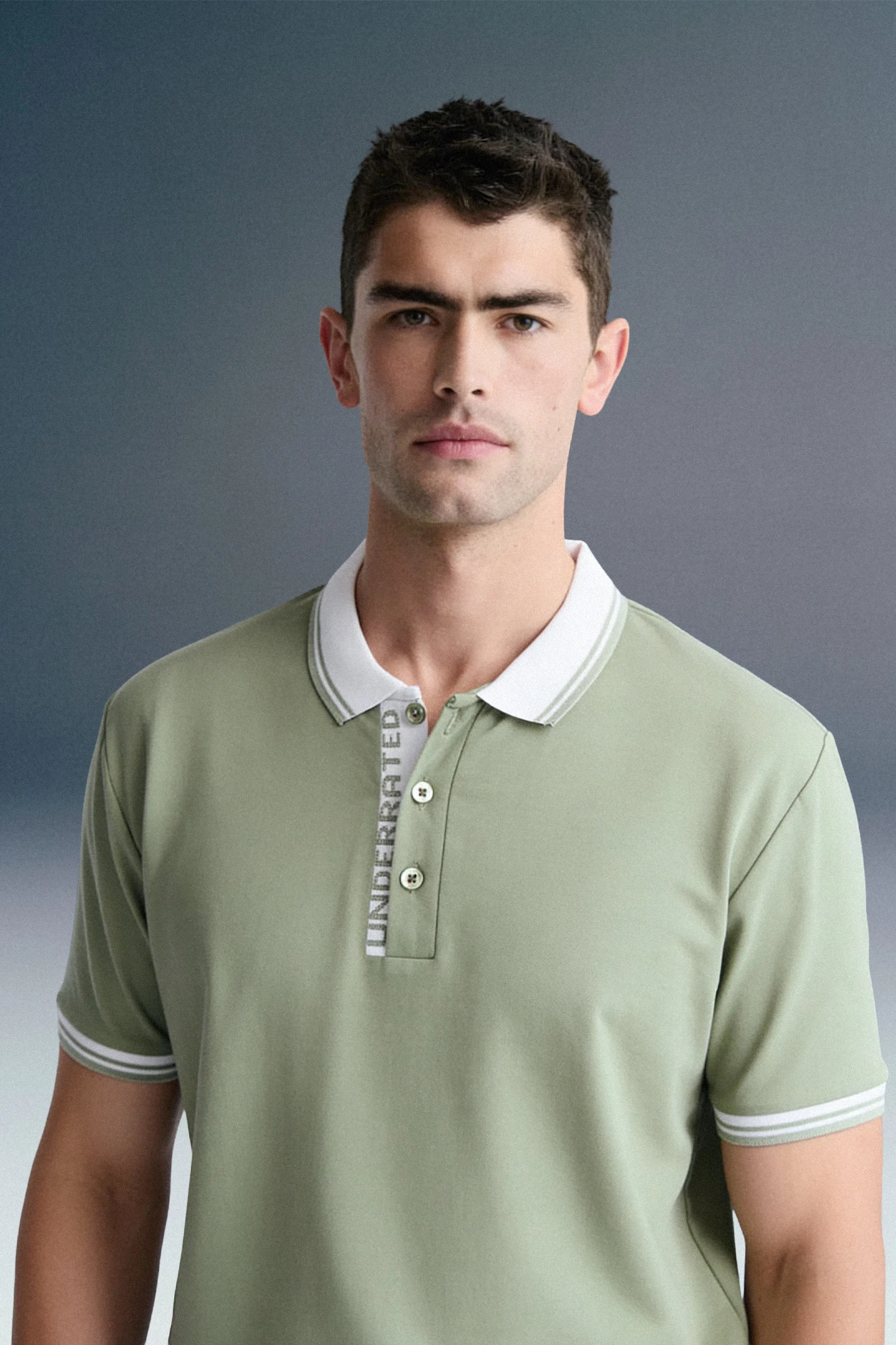 A medium close-up, front-facing shot of a different man looking forward, wearing an olive green polo shirt with a contrasting white collar and white sleeve cuffs.
