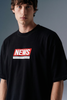A close-up, angled front shot from the chest up of a man looking to the side, highlighting the boxy fit and red box-logo graphic on his black T-shirt.
