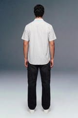 Person wearing a white striped shirt and black pants against a gray background