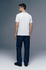 Full-length rear view of a man looking back over his shoulder, wearing a white polo shirt with an olive green collar, paired with dark navy blue trousers.