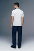 Full-length rear view of a man looking back over his shoulder, wearing a white polo shirt with an olive green collar, paired with dark navy blue trousers.