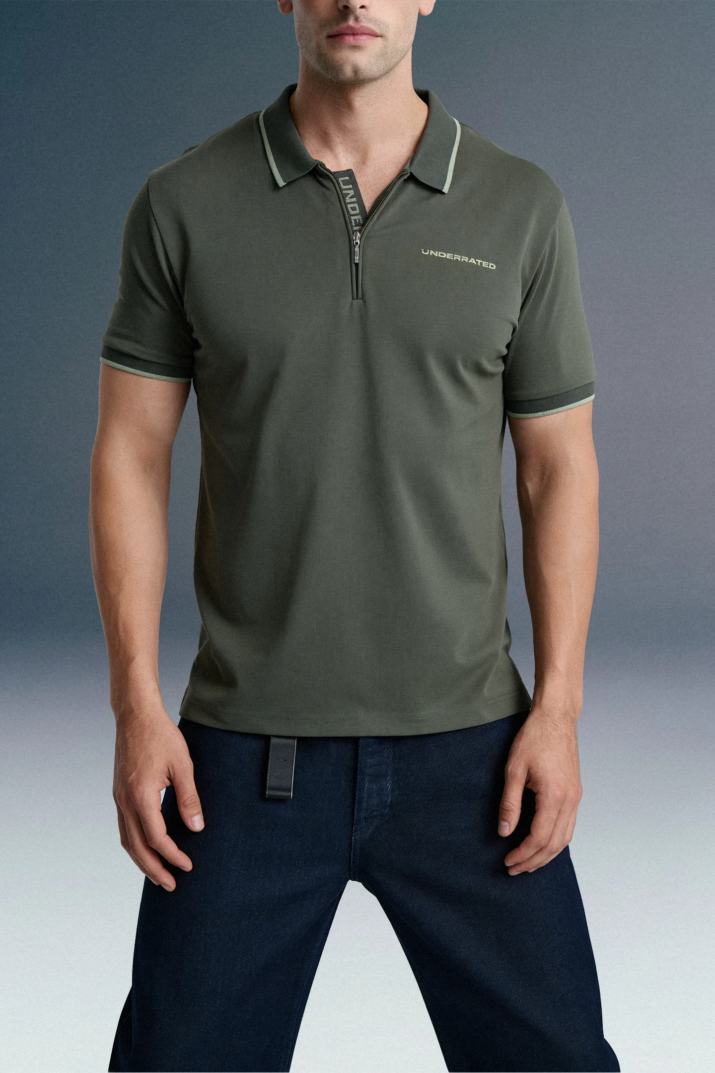 Front view from the waist up of a man wearing a dark olive green polo shirt with subtle chest branding, paired with dark blue jeans.