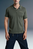 Front view from the waist up of a man wearing a dark olive green polo shirt with subtle chest branding, paired with dark blue jeans.