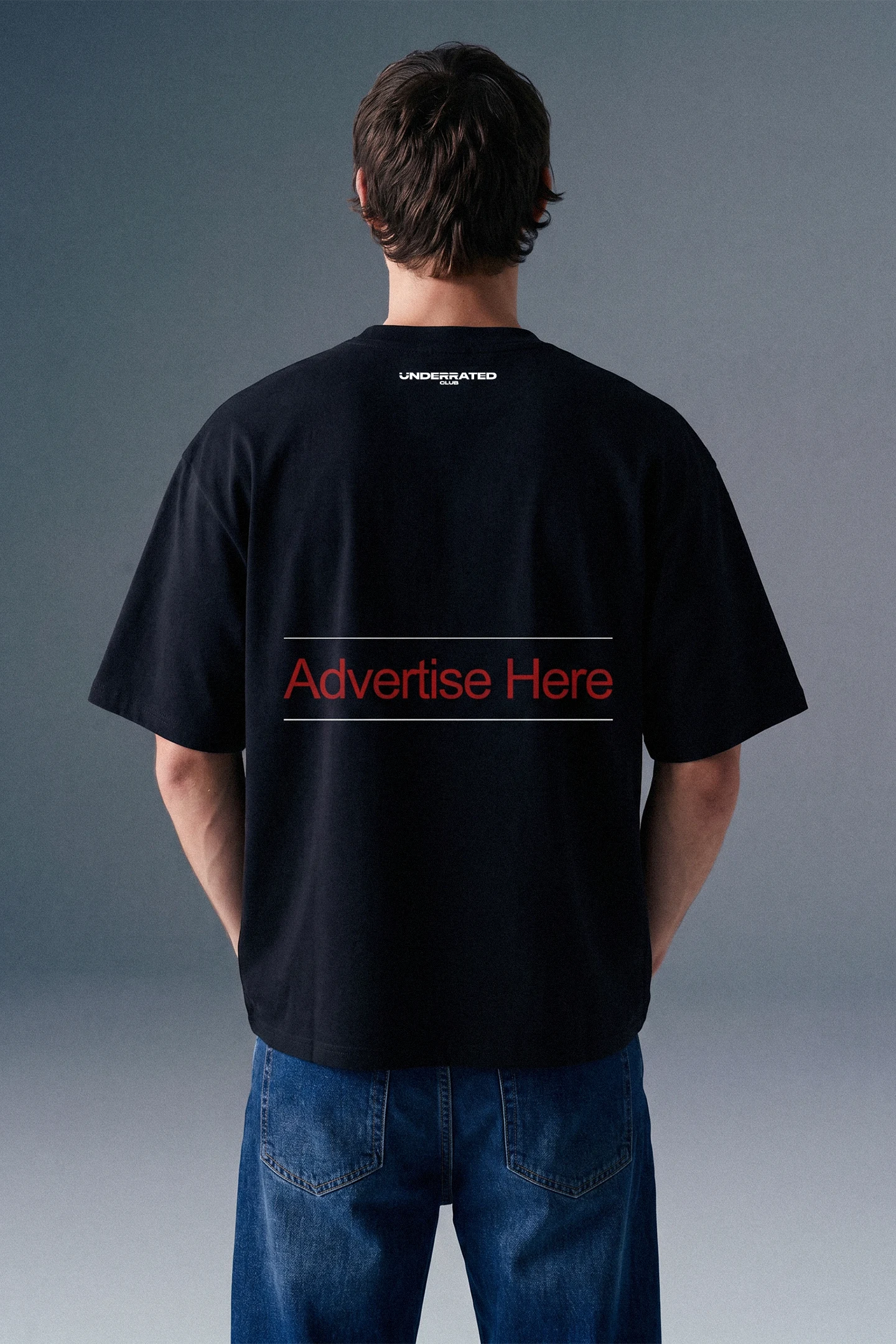 Rear view from the waist up of a man showing the back design of a black oversized T-shirt, which features subtle branding text printed across the upper back shoulders.