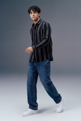 Man wearing a black striped shirt, blue jeans, and white sneakers on a gray background