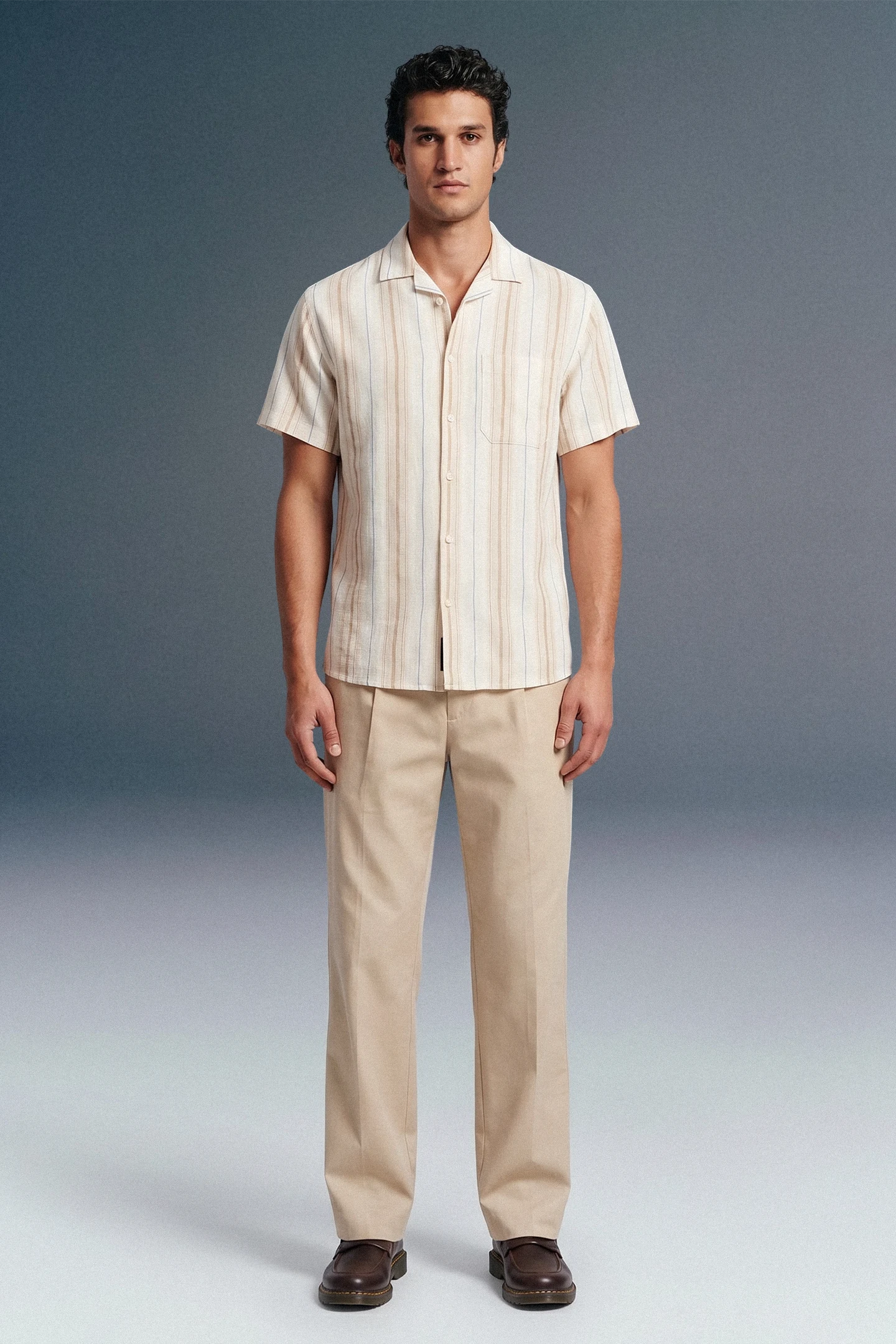 Man wearing a striped shirt and beige pants against a plain background