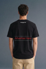 Rear view from the shoulders up of a man looking forward, highlighting the back neckline and branding details on the upper portion of a black T-shirt.