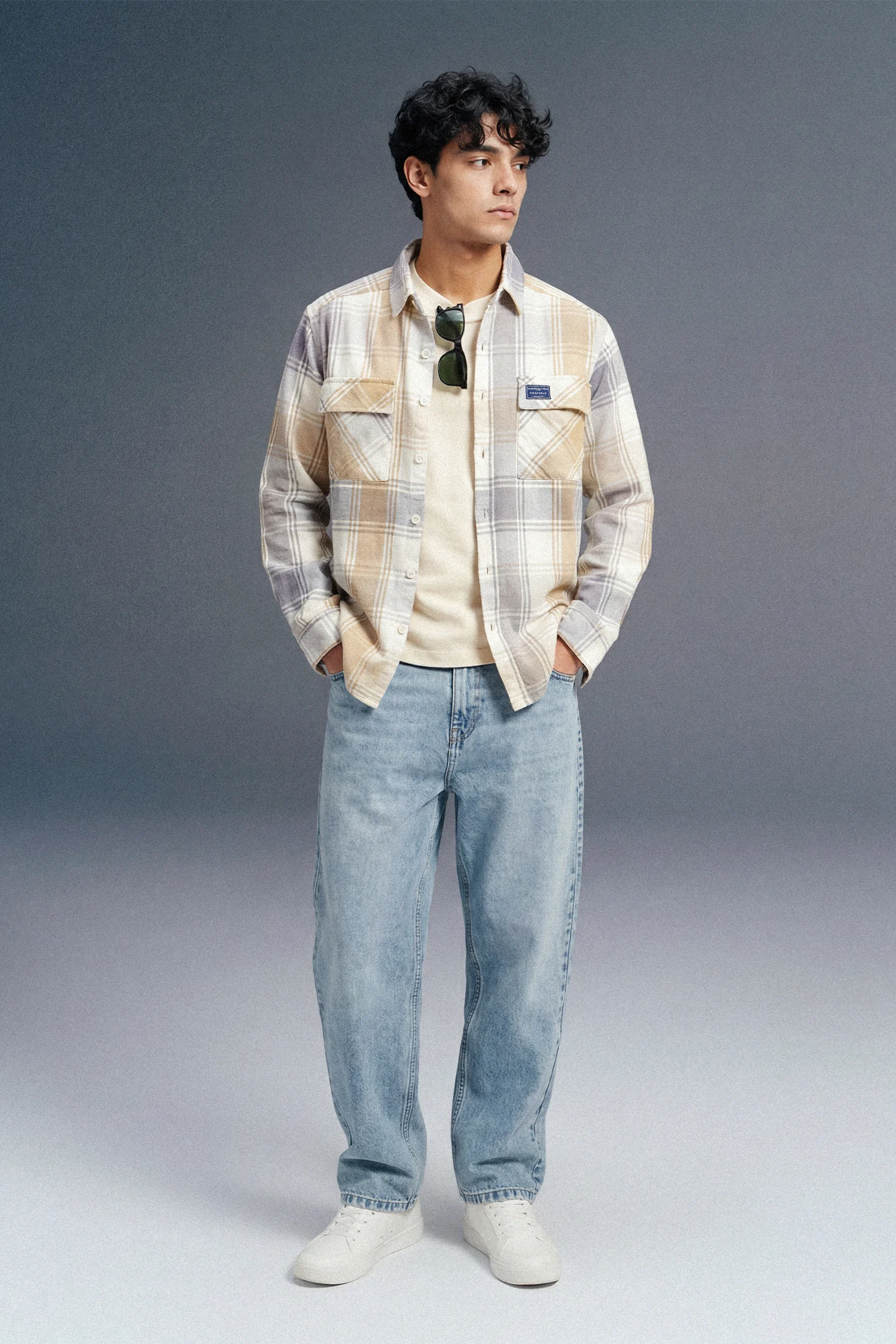 Man wearing a plaid shirt and jeans against a gray background