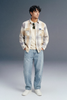 Man wearing a plaid shirt and jeans against a gray background