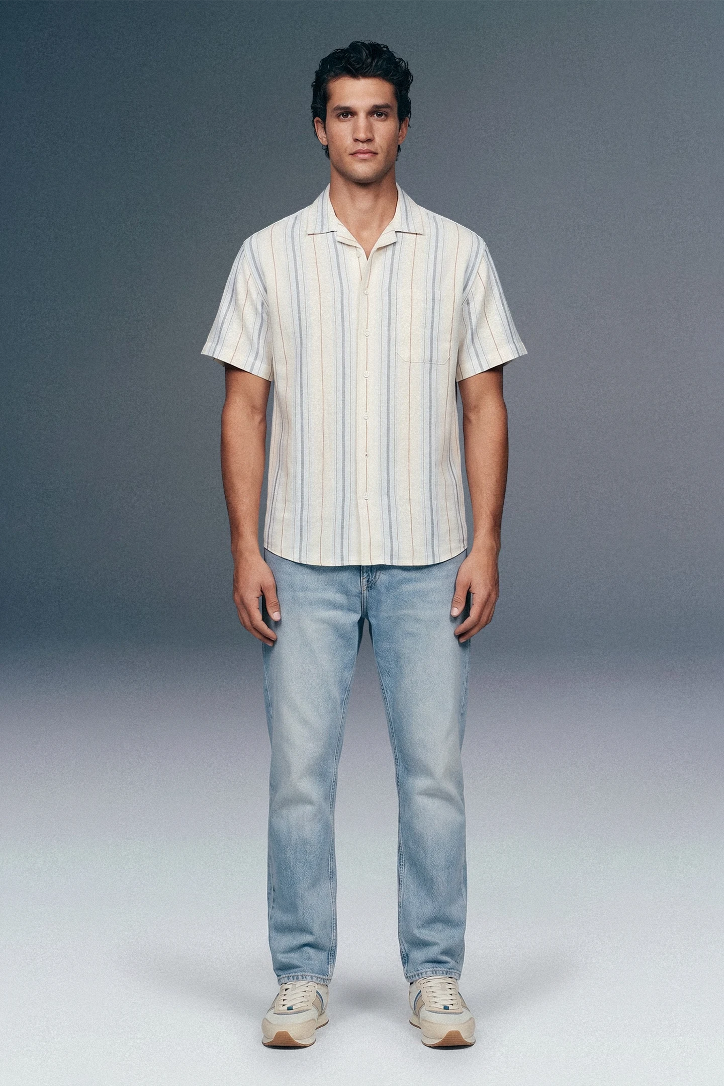 Man wearing a striped shirt and jeans against a plain background