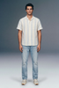 Man wearing a striped shirt and jeans against a plain background