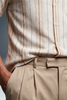 Close-up of a person wearing a beige striped shirt and khaki pants against a gray background