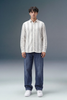 Man wearing a striped shirt and jeans standing against a gray background