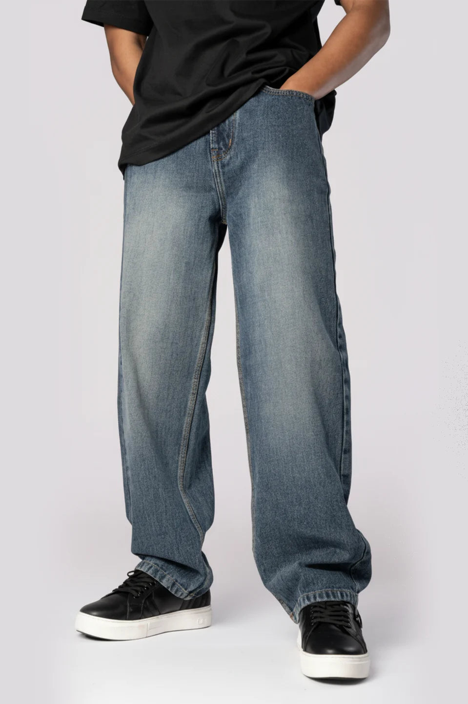 Person wearing loose-fitting, light-wash blue jeans and black sneakers against a white background.