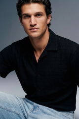Man wearing a black shirt and light blue jeans against a gray background