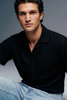 Man wearing a black shirt and light blue jeans against a gray background