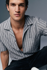 Man wearing a striped shirt with open collar against a gray background