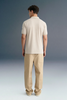 Rear view from the waist up of a man standing still against a grey studio background, highlighting the back structure and shoulders of a dark navy blue polo shirt.