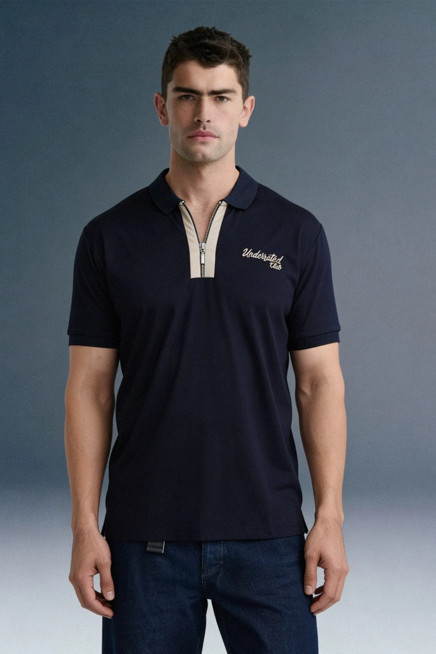 Front view from the waist up of a man looking forward, wearing a navy blue polo shirt with a contrasting beige or checkered inner placket and collar detailing.
