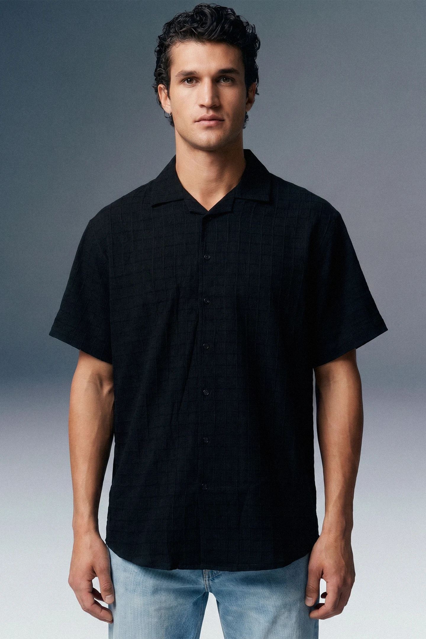 Man wearing a black short-sleeve shirt against a gray background