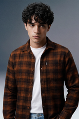 Man wearing a brown plaid shirt over a white t-shirt against a gray background
