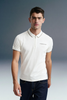 Three-quarter front shot from the waist up of a man looking forward, wearing an off-white polo shirt with a thin dark stripe on the collar, paired with dark blue jeans.