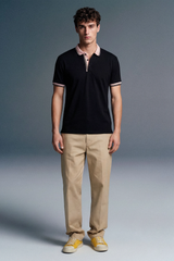 Full-length front view of a man standing and facing forward, wearing a open-collar black polo shirt, khaki trousers, and yellow shoes.