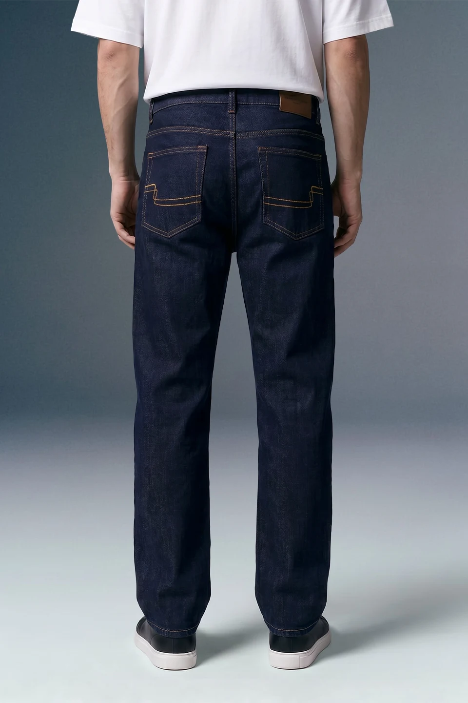 Person wearing dark blue jeans with a plain background