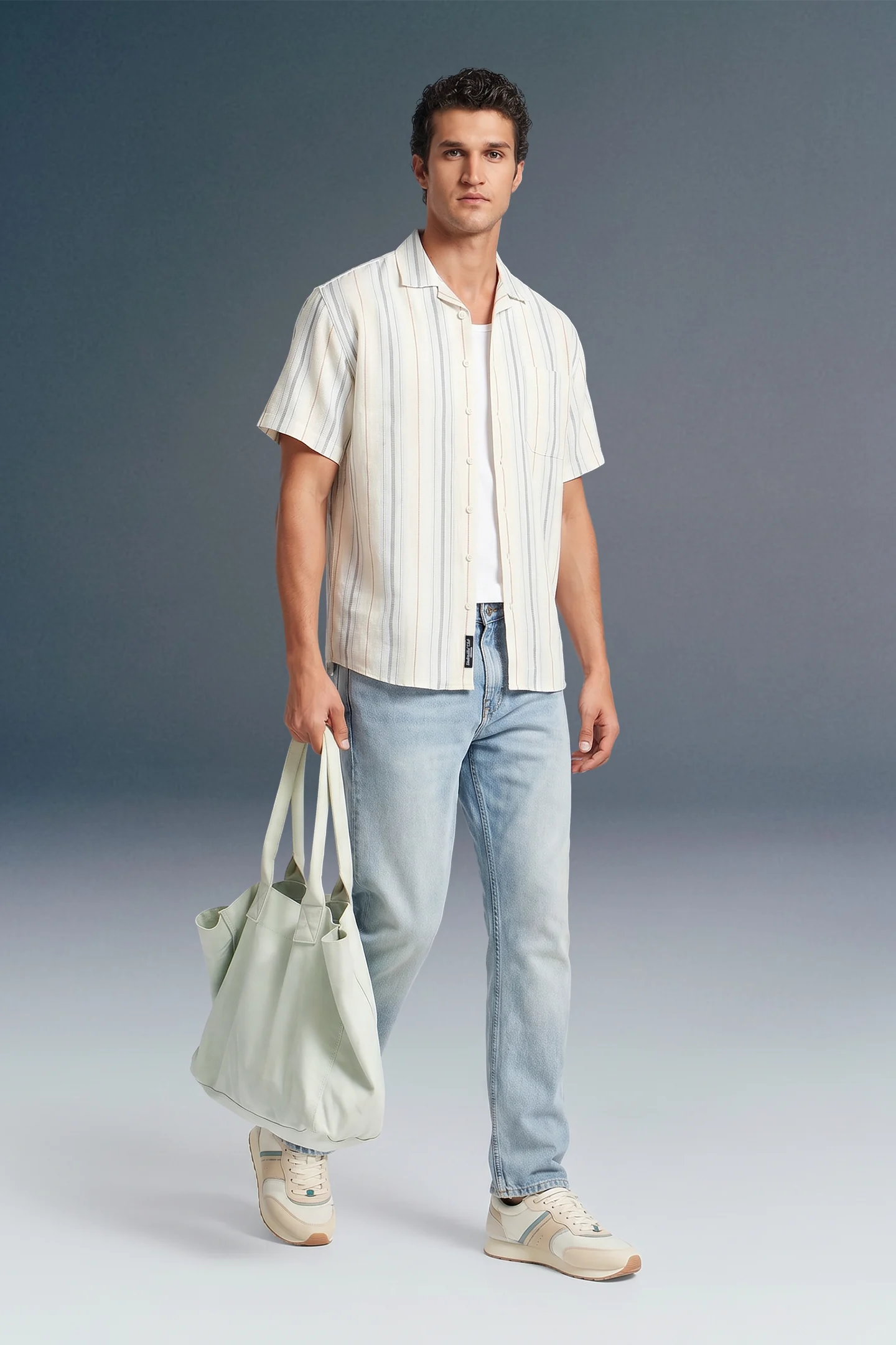 Man wearing a white striped shirt and light blue jeans, holding a light green bag against a gray background