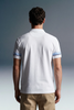 Rear view of a man with dark, wavy hair wearing a white polo shirt and khaki trousers. The short sleeves of the polo feature a repeating blue graphic pattern or text running horizontally around the cuffs.
