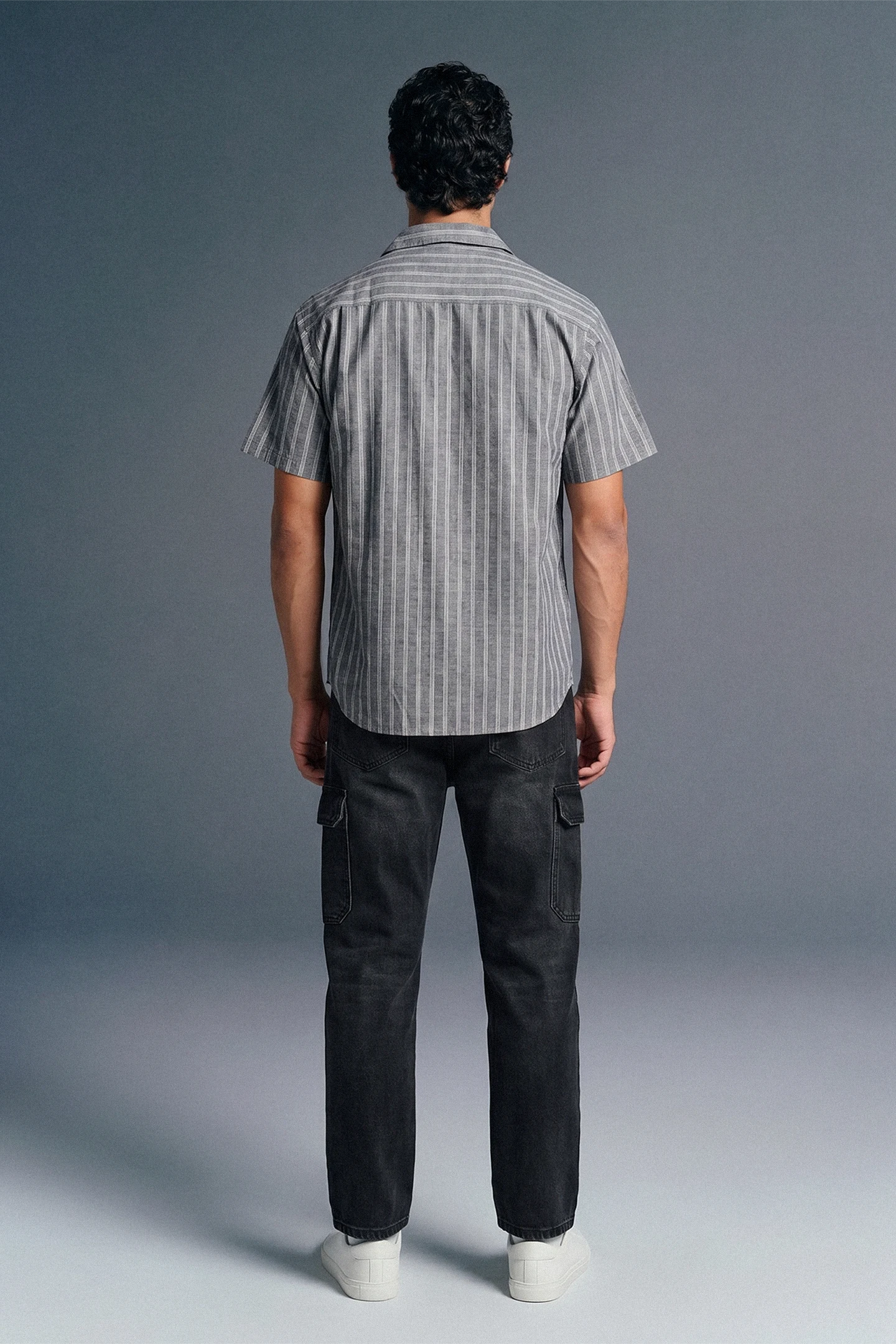 Man wearing a striped shirt and dark pants from behind on a gray background
