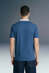 Rear view from the waist up of a man wearing a slate blue polo shirt with a contrasting white collar.