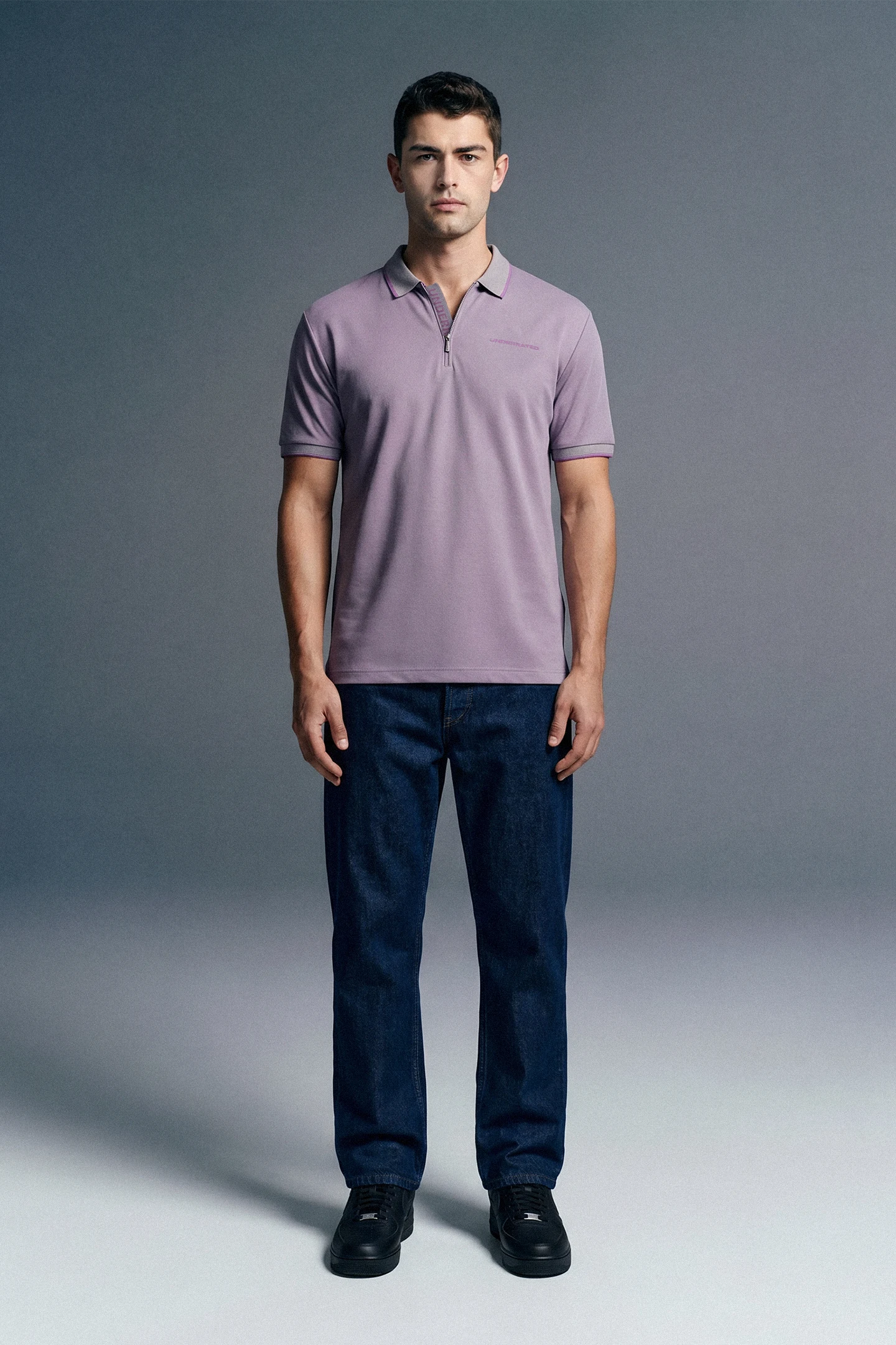 Full-length front view of a man standing still, wearing a light lavender polo shirt paired with dark blue trousers.